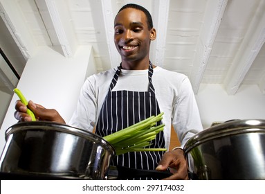 Close Up Of A Young Black Man Wearing An Apron And Cooking At Home. He Is In A Domestic Kitchen And Preparing A Vegetarian Meal.