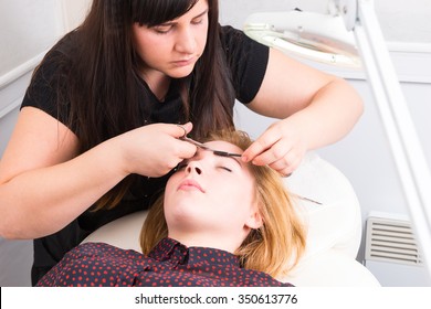 Close Up Of Young Blond Woman Lying Down With Eyes Closed And Having Eyebrows Trimmed By Esthetician Using Scissors And Mascara Brush In Salon Spa