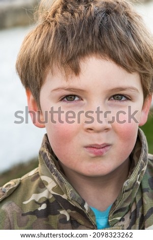 close up of Young Boy with blonde hair and brown eyes age 8 with Army Jacket and messy haircut