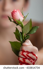 Close Up of Young Boy Clutching Pink Rose in Blood Covered Fist with Blood Seeping Out Through Knuckles - Passion, Sacrifice Concept Image with Diffuse Boy in Background
