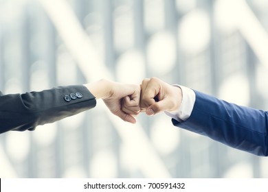Close up of young businessman and businesswoman making a fist bump on building background. Business people wear suit do a fist pump together after good deal. Business success and teamwork concept.
