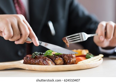 Close Up Of  Young Businessman Eating Rib Steak On Wooden Tray At Restaurant.