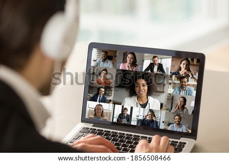 Close up young businessman in headphones holding online video call conference with african american female team leader and diverse colleagues using computer application, distant working communication.