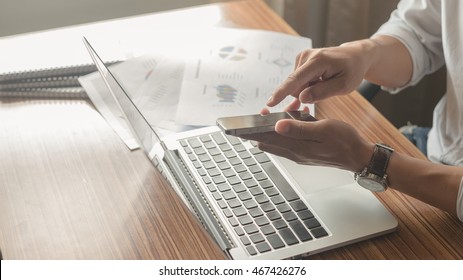 Close Up Young Businessman Planing Documents ,charts At Office. Image Of Worksheet And Chart Of Him Business.and Hand Push Labtop Botton. Have Smart Phone On Hand. Now Press Button On Smartphone.