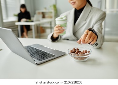 Close Up Of Young Businesswoman Picking Sweet Snacks While Working At Desk In Office, Copy Space