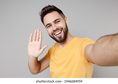 Close Up Young Caucasian Smiling Bearded Attractive Man In Casual Yellow Basic T-shirt Doing Selfie Shot On Mobile Phone Waving Hand Palm Greeting Someone Isolated On Grey Background Studio Portrait