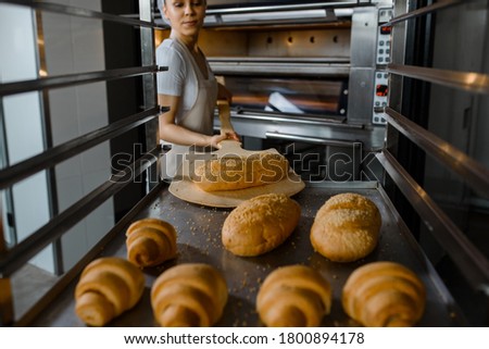 Close up of young caucasian woman baker putting the fresh bread on the shelves/rack at baking manufacture factory. Tasty bread bakery factory concept.