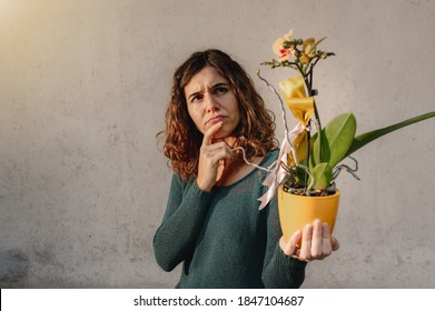 Close up young caucasian woman holding a yellow potted orchid plant. Worried face because inexperienced gardener. - Shutterstock ID 1847104687