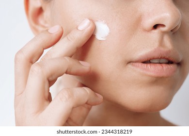 Close up of a young caucasian woman touching the face with her hand applying a smearof cream on the skin isolated on a white background. Nourishing moisturizing cream. Cosmetology and beauty