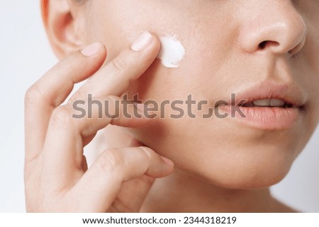 Close up of a young caucasian woman touching the face with her hand applying a smearof cream on the skin isolated on a white background. Nourishing moisturizing cream. Cosmetology and beauty
