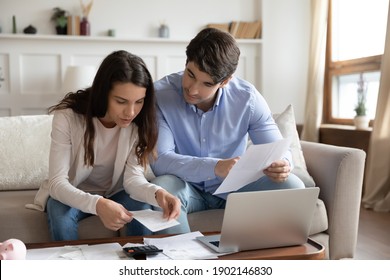 Close up young couple checking mortgage or loan agreement, financial documents together, using laptop and calculator, sitting on couch at home, focused wife and husband calculating domestic bills
