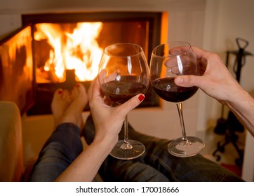 Close Up Of Young Couple Drinking Wine In Front Of An Open Wood Fire. 