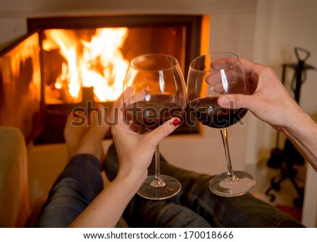 close up of young couple drinking wine in front of an open wood fire. 