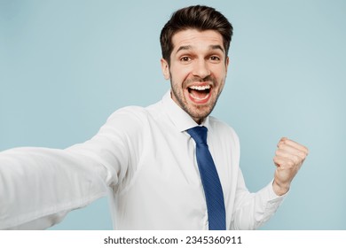 Close up young employee business man corporate lawyer wears classic formal shirt tie work in office do selfie shot pov on mobile cell phone do winner gesture isolated on plain blue background studio