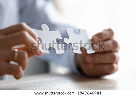 Close up young entrepreneur putting different parts of puzzles together, making business decision, finding creative logical problem solution or developing strategy brainstorming alone in office.
