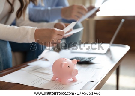 Close up of young family sit at desk manage household finances save money in piggy bank for future, couple consider home financial paperwork documents together, feel economical about expenses