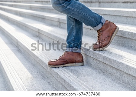 Close up a Young fashion man's legs in blue jeans and brown boots on the walk down the concrete stairs, lifestyle men's fashion