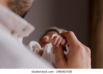Close Up Of Young Father Holding The Hand Of His Newborn Baby At Home - Happy Hispanic Father Holding His Baby In His Arms