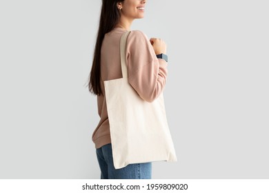 Close Up Of Young Female Consumer Holding Blank White Eco Tote Bag, Posing Standing Over Studio Background. Lady Carrying Flax Tote Shopper Handbag. Eco-Friendly Lifestyle, Stop Using Plastic Concept