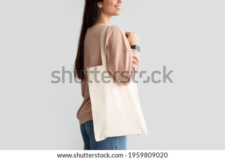 Close Up Of Young Female Consumer Holding Blank White Eco Tote Bag, Posing Standing Over Studio Background. Lady Carrying Flax Tote Shopper Handbag. Eco-Friendly Lifestyle, Stop Using Plastic Concept