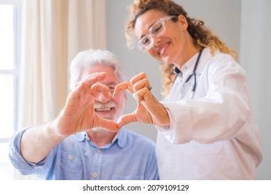 Close Up Of Young Female Doctor And Senior Man Showing Heart Sign With Hand At Home. Doctor Helping Senior Patient And Giving Care. Elderly Medical Health Care.