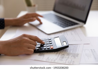 Close up of young female electronic bank client using calculator in paperwork with accounts bills before providing payment online by laptop. Woman hands at work table with papers accounting sum to pay