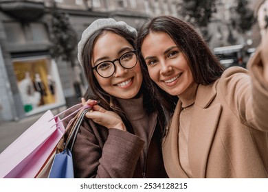 Close up of young female friends with bags standing outdoors urban street city center and taking selfie photo vlogging blogging online on smartphone cellphone together - Powered by Shutterstock