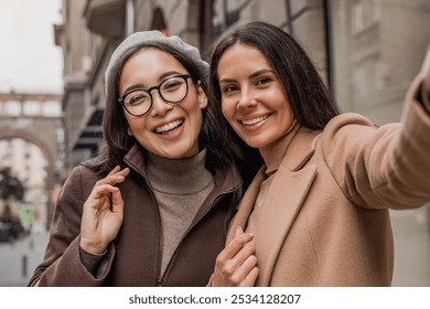 Close up of young female friends standing outdoors urban street city center and taking selfie photo vlogging blogging online on smartphone cellphone together - Powered by Shutterstock