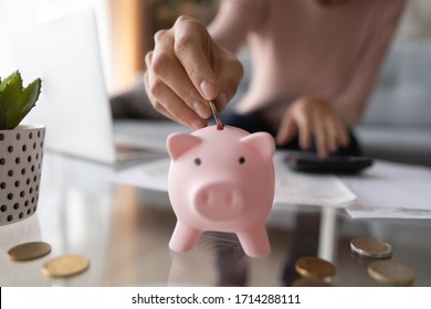 Close up young female putting coin in piggy bank. Woman saving money for household payments, utility bills, calculating monthly family budgets, making investments or strategy for personal savings.
