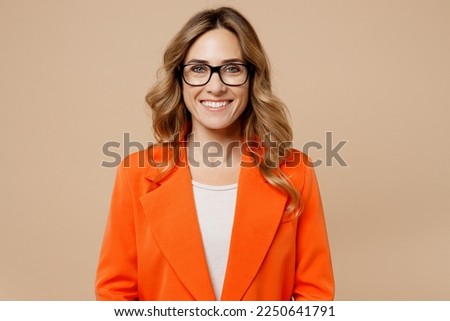 Close up young fun happy successful employee business woman corporate lawyer 30s wearing classic formal orange suit glasses work in office look camera isolated on plain beige color background studio
