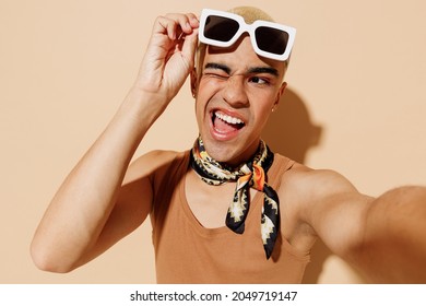 Close Up Young Fun Trendy Blond Latin Gay Man In Beige Tank Shirt Neck Scarf Sunglasses Doing Selfie Shot Pov On Mobile Phone Look Aside Blink Isolated On Plain Light Ocher Color Background Studio.