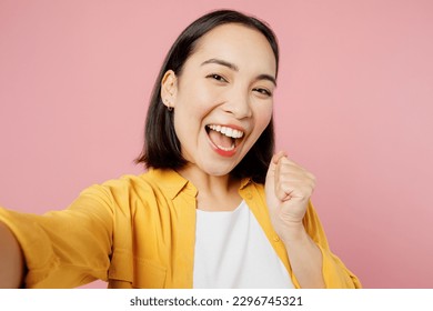 Close up young fun woman of Asian ethnicity wear yellow shirt white t-shirt doing selfie shot pov on mobile cell phone do winner gesture isolated on plain pastel light pink background studio portrait - Powered by Shutterstock