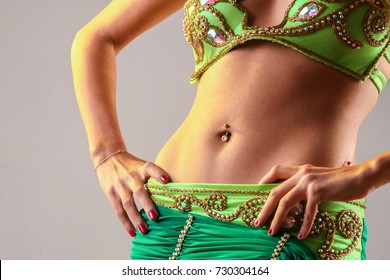 Close up of a young girl in belly dance costume, stomach with jewel piercing and hands resting on her hips.