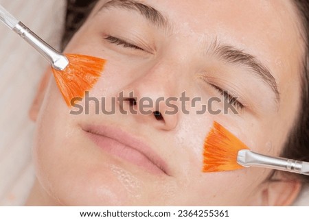 Close up of young girls face getting a facial gel peeling mask with the help of two brushes. Professional procedure in a beauty salon, skincare and cosmetology spa concept