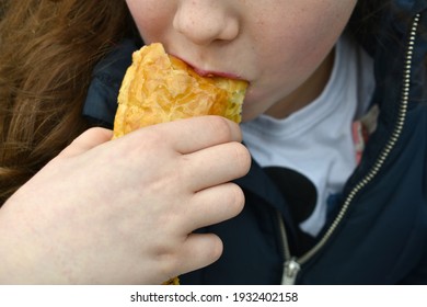 Close Up Of Young Girl's Mouth Taking A Bite From A Pastry Snack.  The Child's Hand Is Holding The Sausage Roll Putting It To Her Lips, Outside