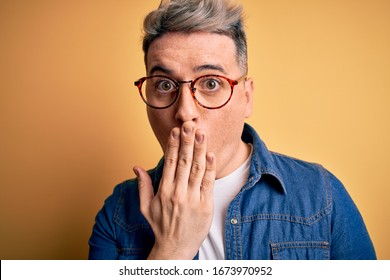 Close Up Of Young Handsome Modern Man Wearing Glasses And Denim Jacket Over Yellow Background Cover Mouth With Hand Shocked With Shame For Mistake, Expression Of Fear, Scared In Silence, Secret 