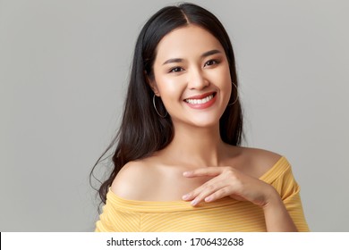 Close up young happy attractive Asian woman wearing yellow showing shoulder dress with sweet smile face isolated on grey background.