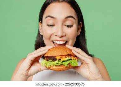 Close up young happy cheerful woman wear white clothes holding eating biting tasty burger isolated on plain pastel light green background. Proper nutrition healthy fast food unhealthy choice concept - Powered by Shutterstock