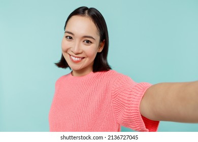 Close Up Young Happy Woman Of Asian Ethnicity 20s In Pink Sweater Doing Selfie Shot Pov On Mobile Phone Isolated On Pastel Plain Light Blue Color Background Studio Portrait. People Lifestyle Concept