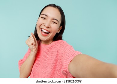 Close Up Young Happy Woman Of Asian Ethnicity 20s In Pink Sweater Do Selfie Shot Pov On Mobile Phone Do Winner Gesture Isolated On Pastel Plain Light Blue Background Studio. People Lifestyle Concept