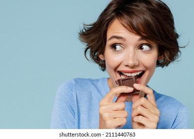 Close up young happy woman in casual sweater hold sweet pink cream donuts biting chocolate bar look camera isolated on plain pastel light blue background studio portrait. People lifestyle food concept