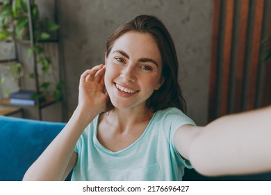 Close Up Young Happy Woman She 20s In Casual Clothes Mint T-shirt Do Selfie Shot Pov On Mobile Cell Phone Hold Face Sit On Blue Sofa Indoor Rest At Home In Own Room Apartment People Lifestyle Concept