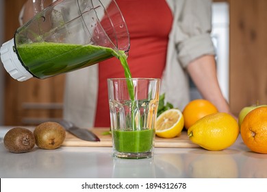 Close Up Of Young Healthy Woman Pouring Fresh Juice In Glass. Girl Pouring A Green Detox Smoothie From Blender To A Tumbler At Home. Woman Prepare Freshly Made Antioxidant Smoothie From Grinder Jar.