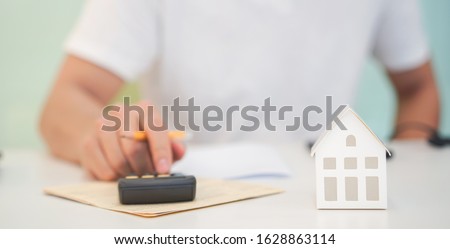 close up young house model with man hand pressing calculator for check and summary expense of home loan mortgage for refinance plan , people lifestyle and work from home and economic inflation concept