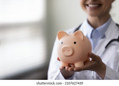 Close up young Indian female general practitioner physician therapist holding piggy bank in hands, recommending saving money for healthcare medical insurance service, copy space for advertising text.