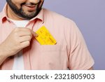 Close up young Indian man he wearing pink shirt white t-shirt casual clothes hold put credit bank card into pocket isolated on plain pastel light purple background studio portrait. Lifestyle concept