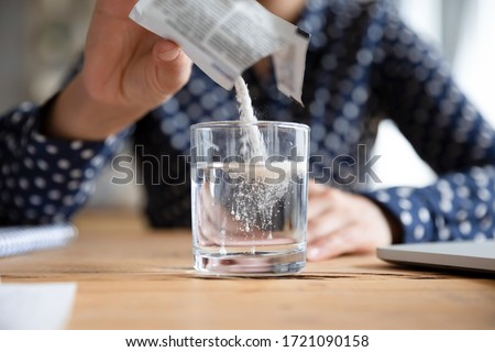 Close up young indian woman pouring soluble anti-influenza powder in glass of water. Sick millennial girl student feeling unwell, relieving grippe fever flu symptoms, high temperature, headache.