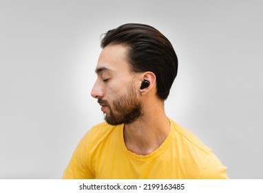 Close Up Of Young Latin Man Ear In Profile With Ear Buds, Wireless Headset, Looking To The Side With Closed Eyes On White Background