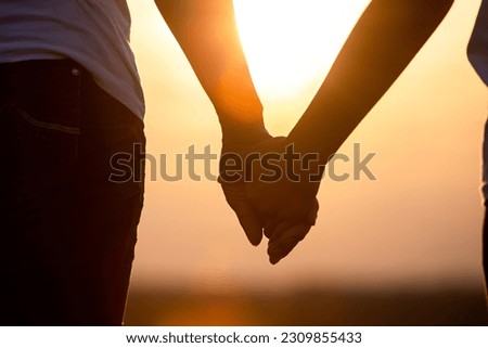 Close up of young love couple silhouette holding hands on sunset background.