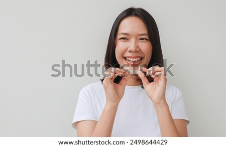close up young lovely asian woman hand holding dental aligner retainer (invisible) on grey background for beautiful teeth content and dental treatment course concept